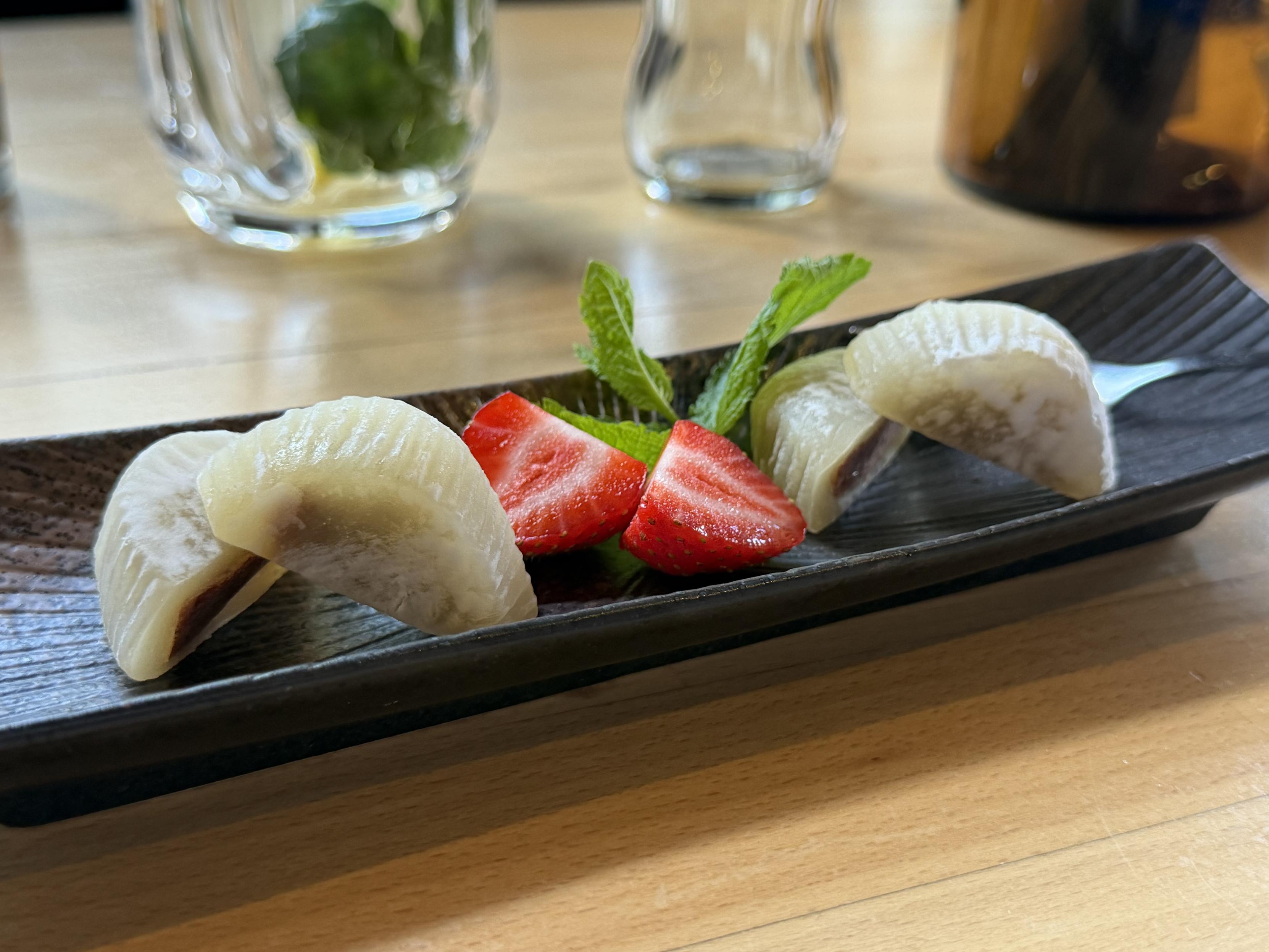 Mochi und Erdbeeren auf einem schwarzen Teller mit Minzblättern.