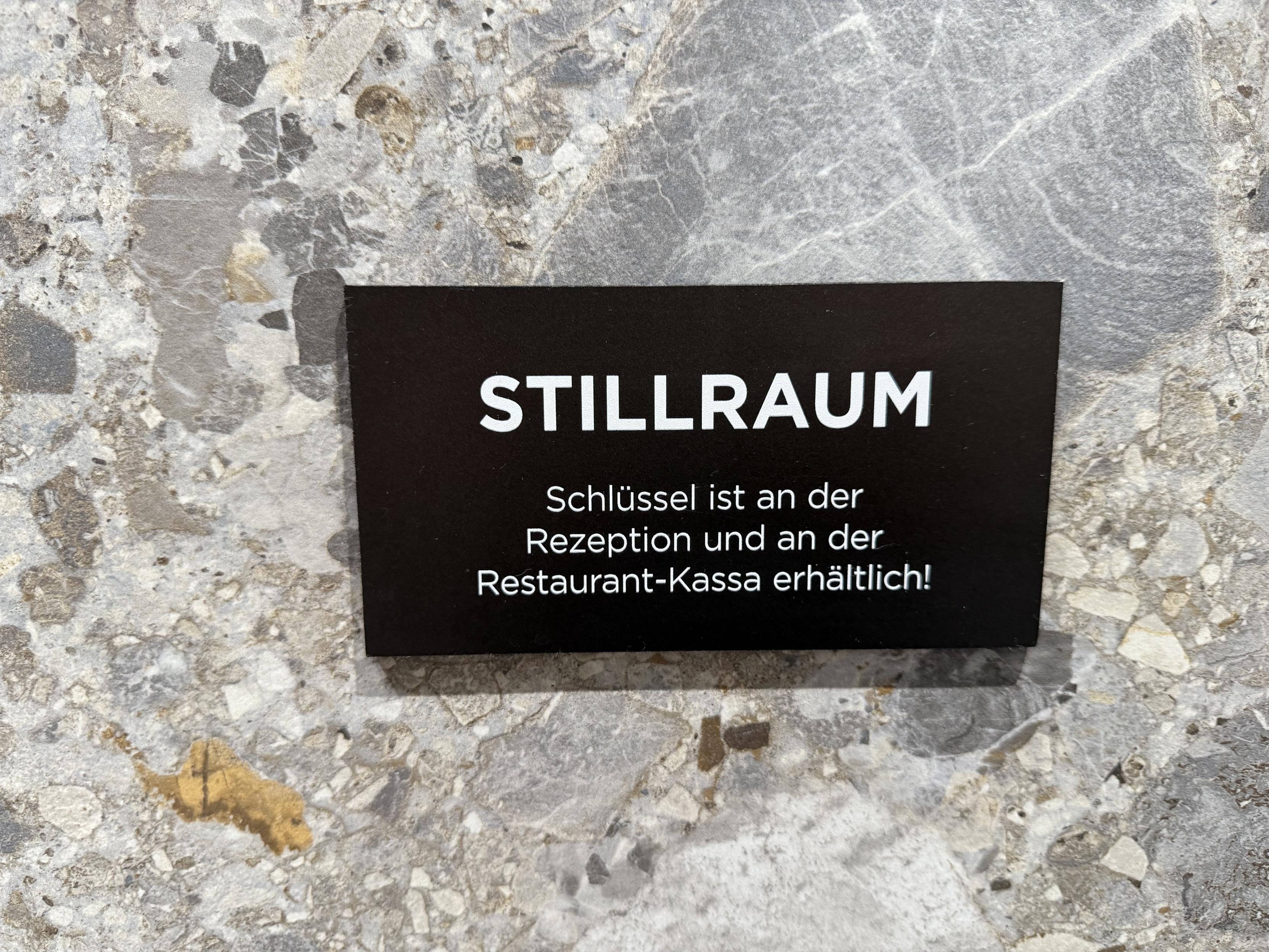 Schwarzes Schild an einer Steinwand: „Stillraum: Schlüssel ist an der Rezeption und an der Restaurantkasse erhältlich!“