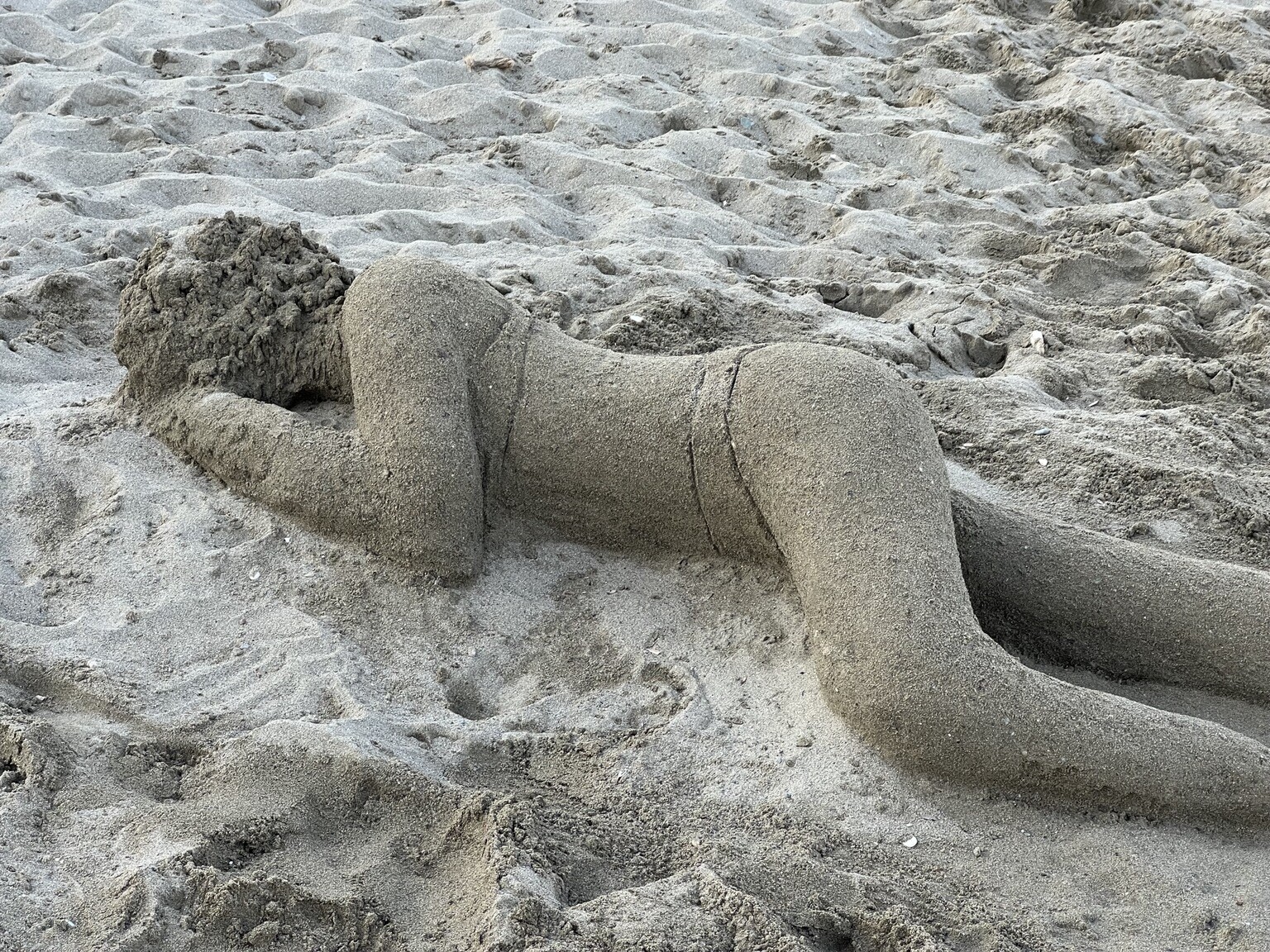 Liegende Frau in Bikini als Sandfigur - von vorne