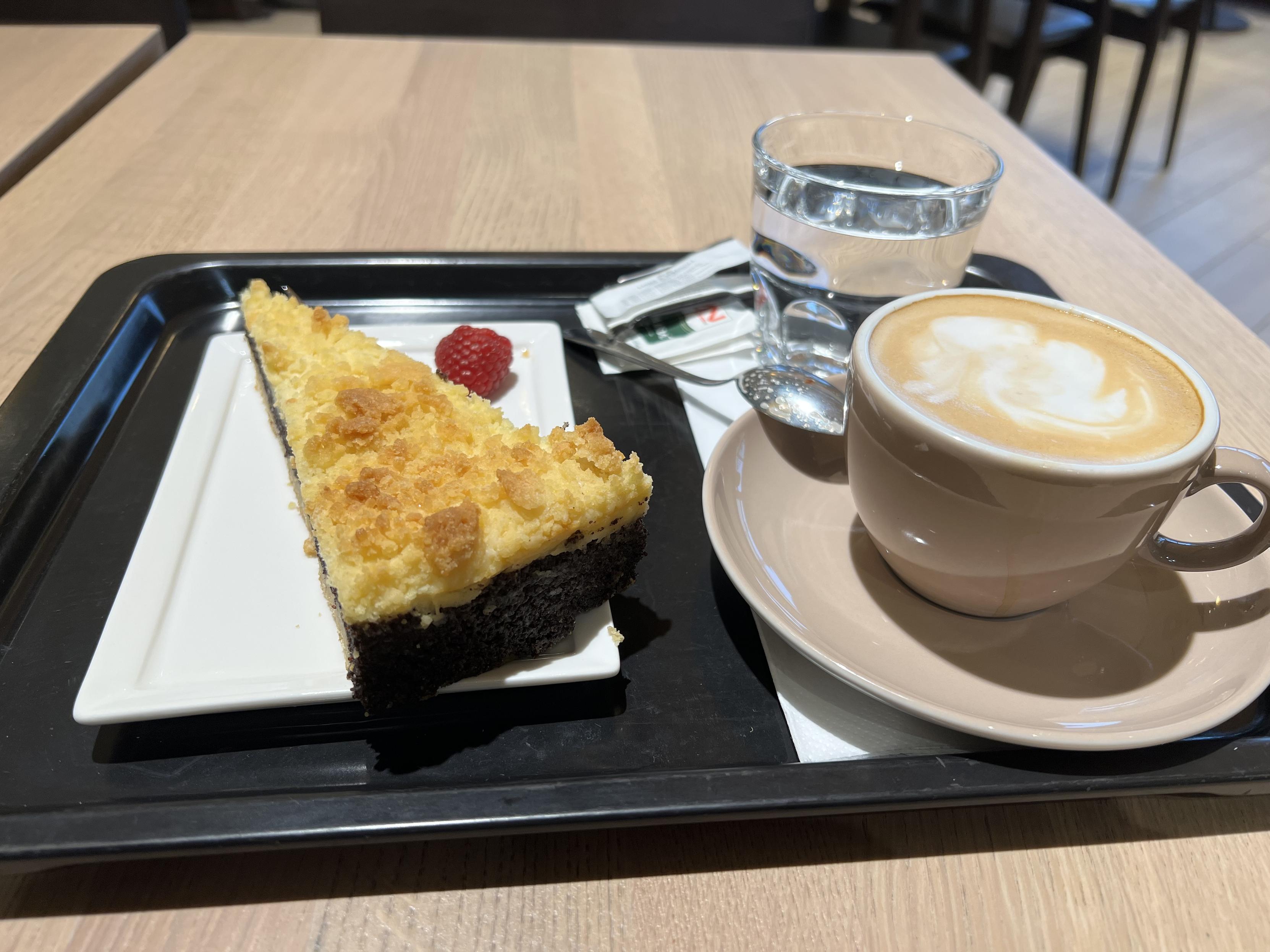 Tablet mit einer Tasse Kaffee, Glas Wasser und einem Mohnkuchen darauf. 