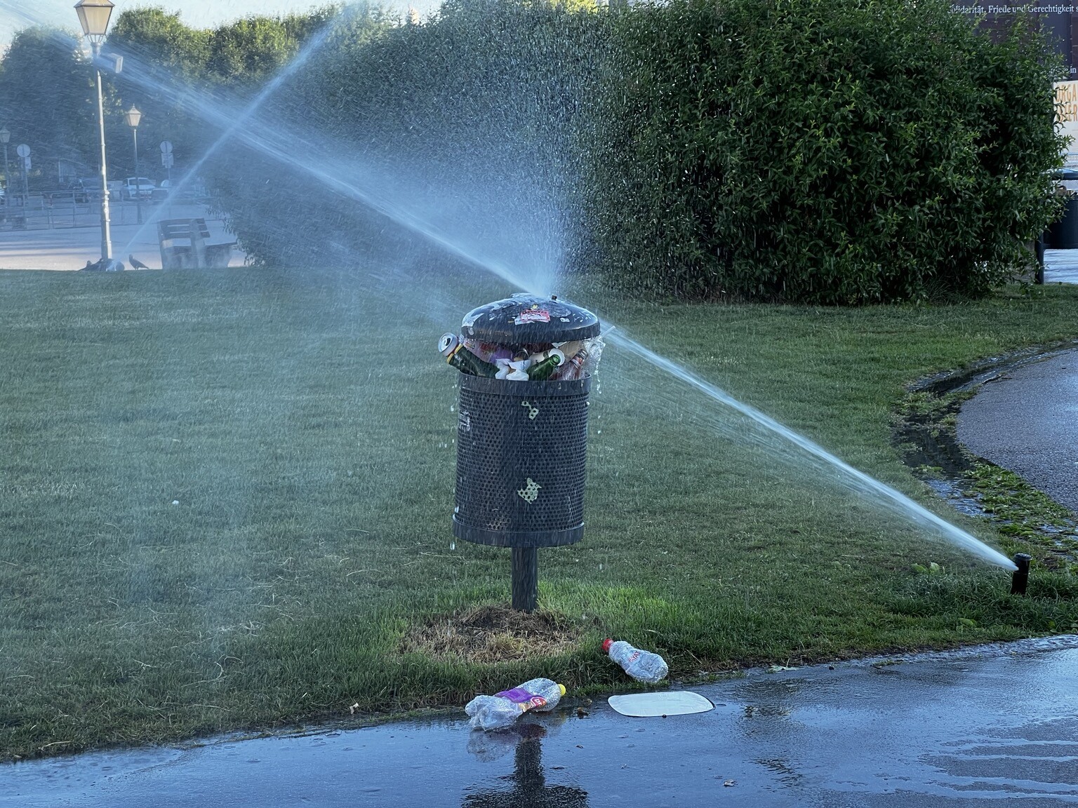 Bodensprinkler im Rasen richtet Wasserstrahl direkt auf Mistkübel