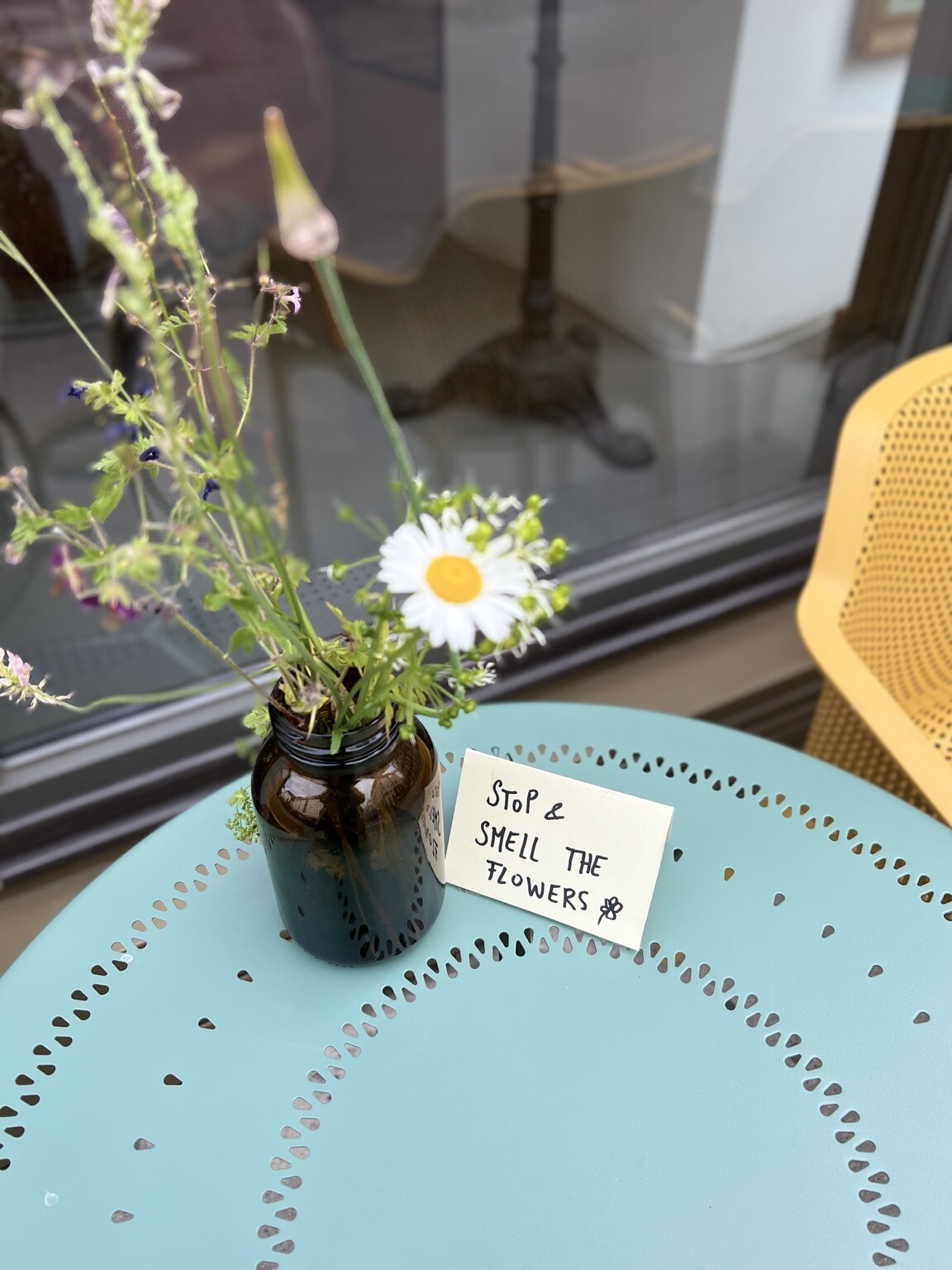 Tischchen mit Blumen in Vase und Schild „Stop and smell the Flowers“