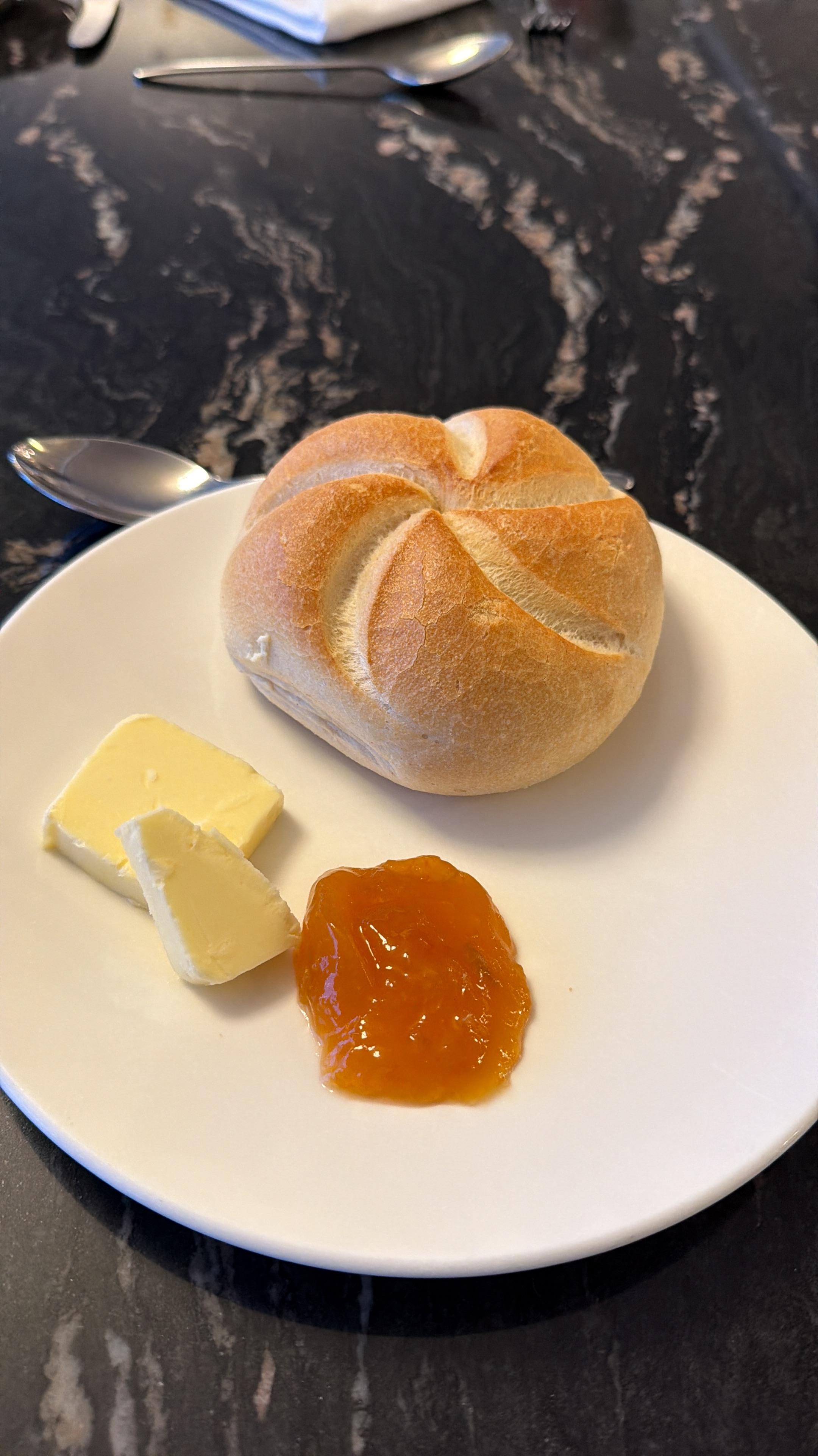 Teller mit Semmel, Stück Butter und einen Batzen Marmelade.