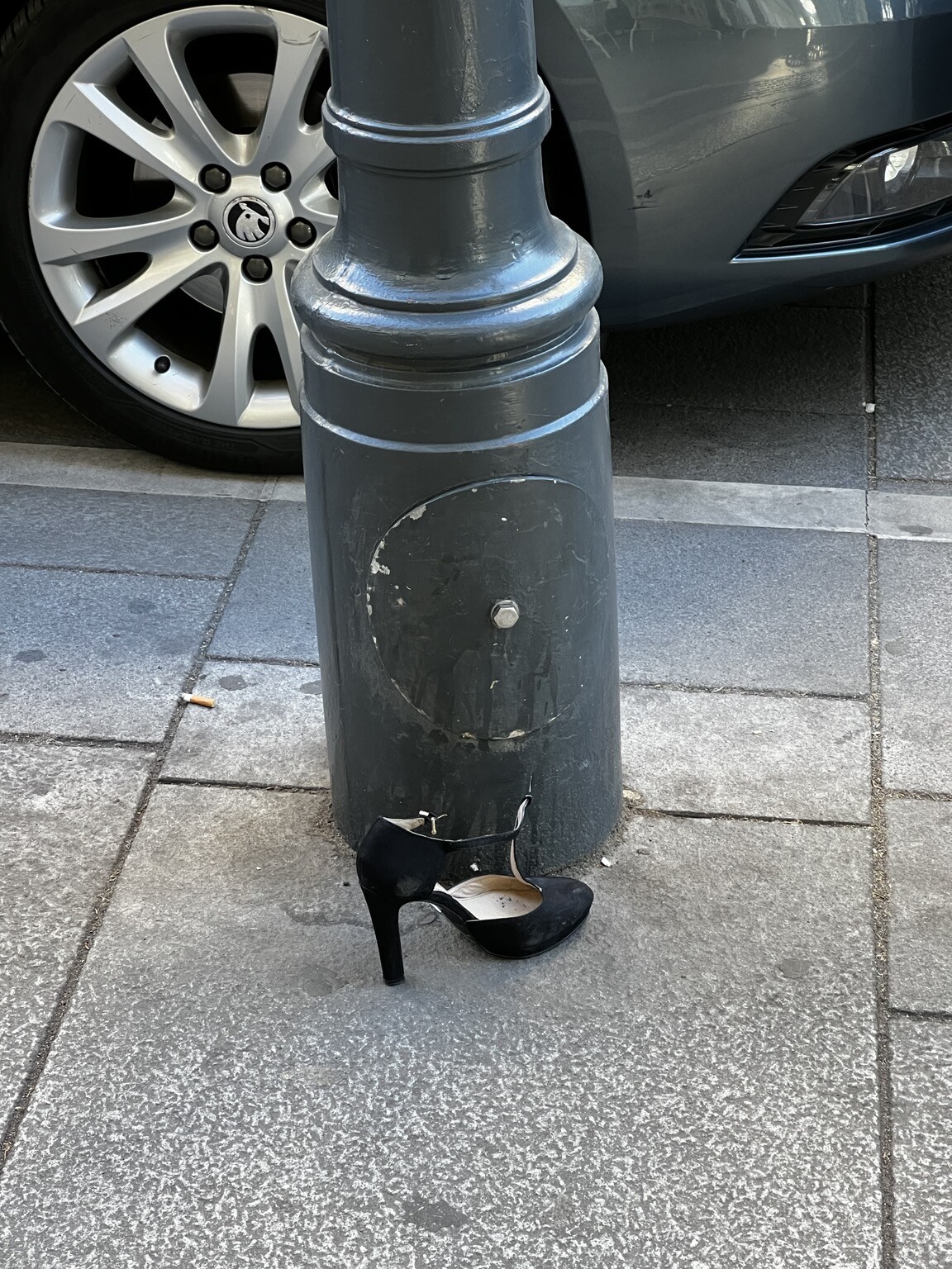 Stöckelschuh auf dem Gehsteig vor Lichtmast stehend.