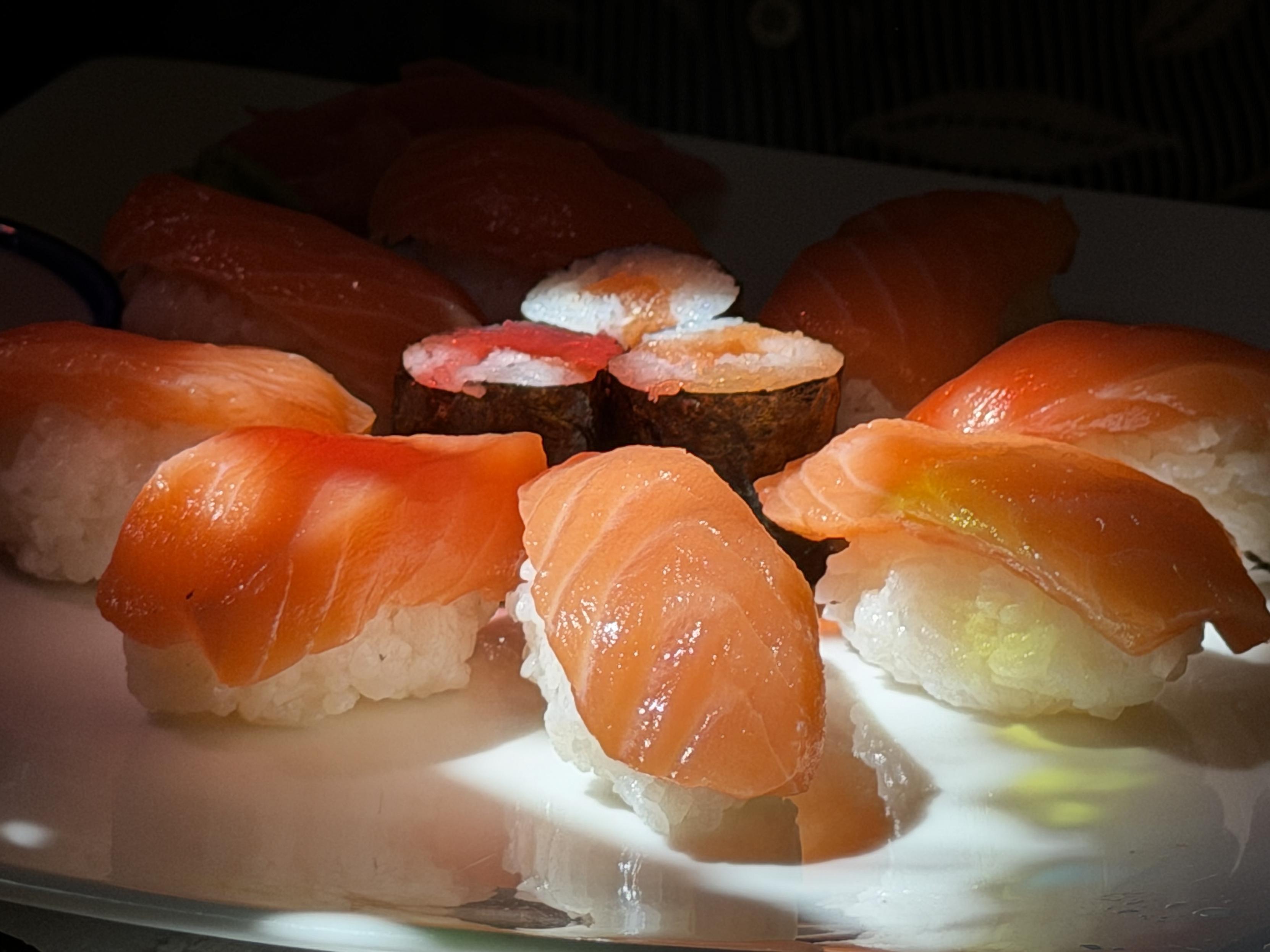 Verschiedene Sushi-Variationen mit Lachs auf einem weißen Teller, teilweise im Schatten.