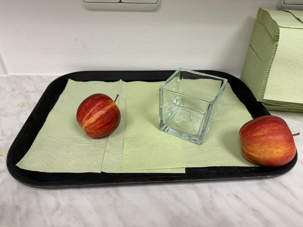 Zwei Äpfel und ein Glas auf einem schwarzen Tablett mit grünen Servietten.