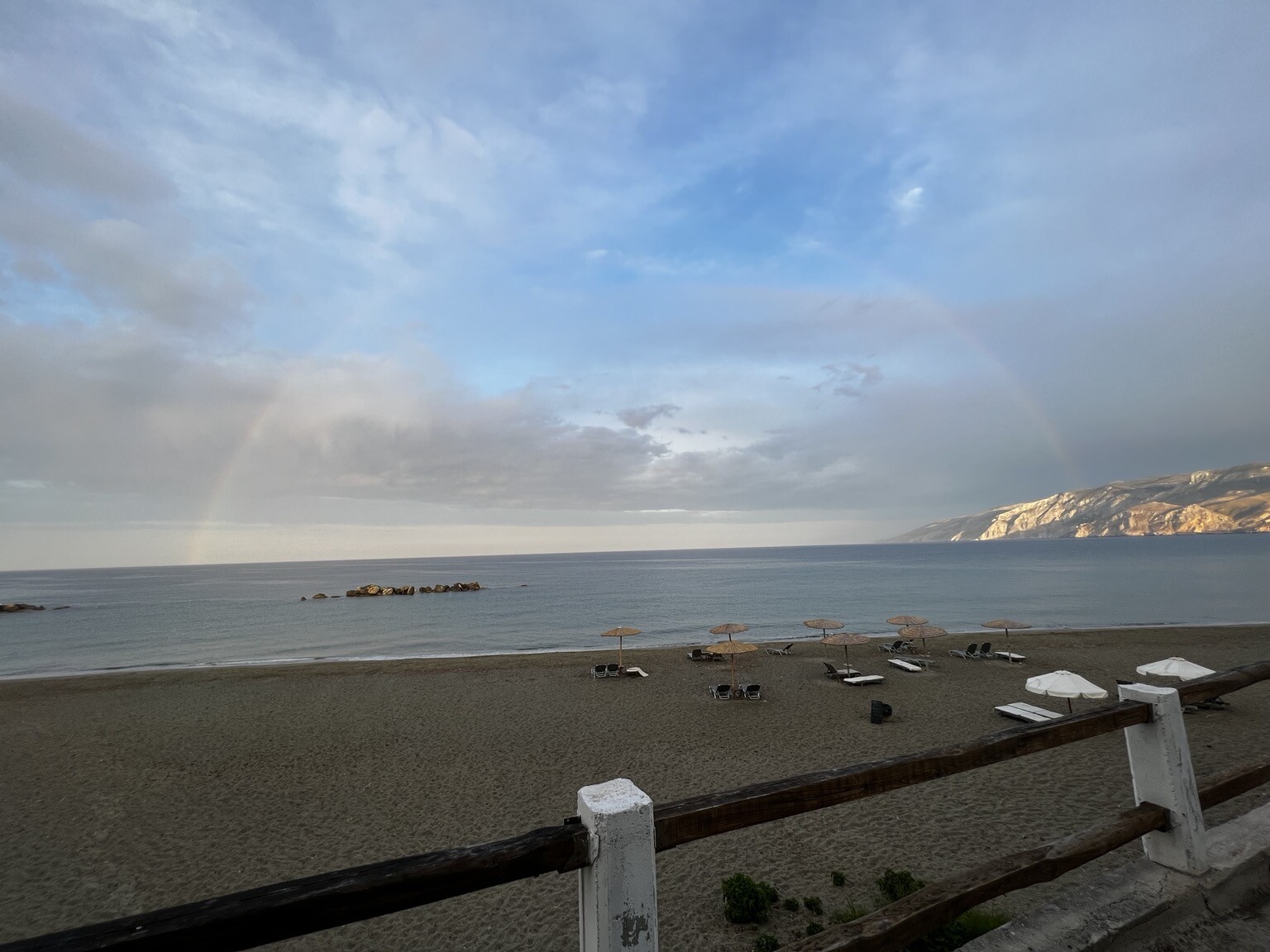 Vollständiger Regenbogen über dem Meer. Davor Strand.