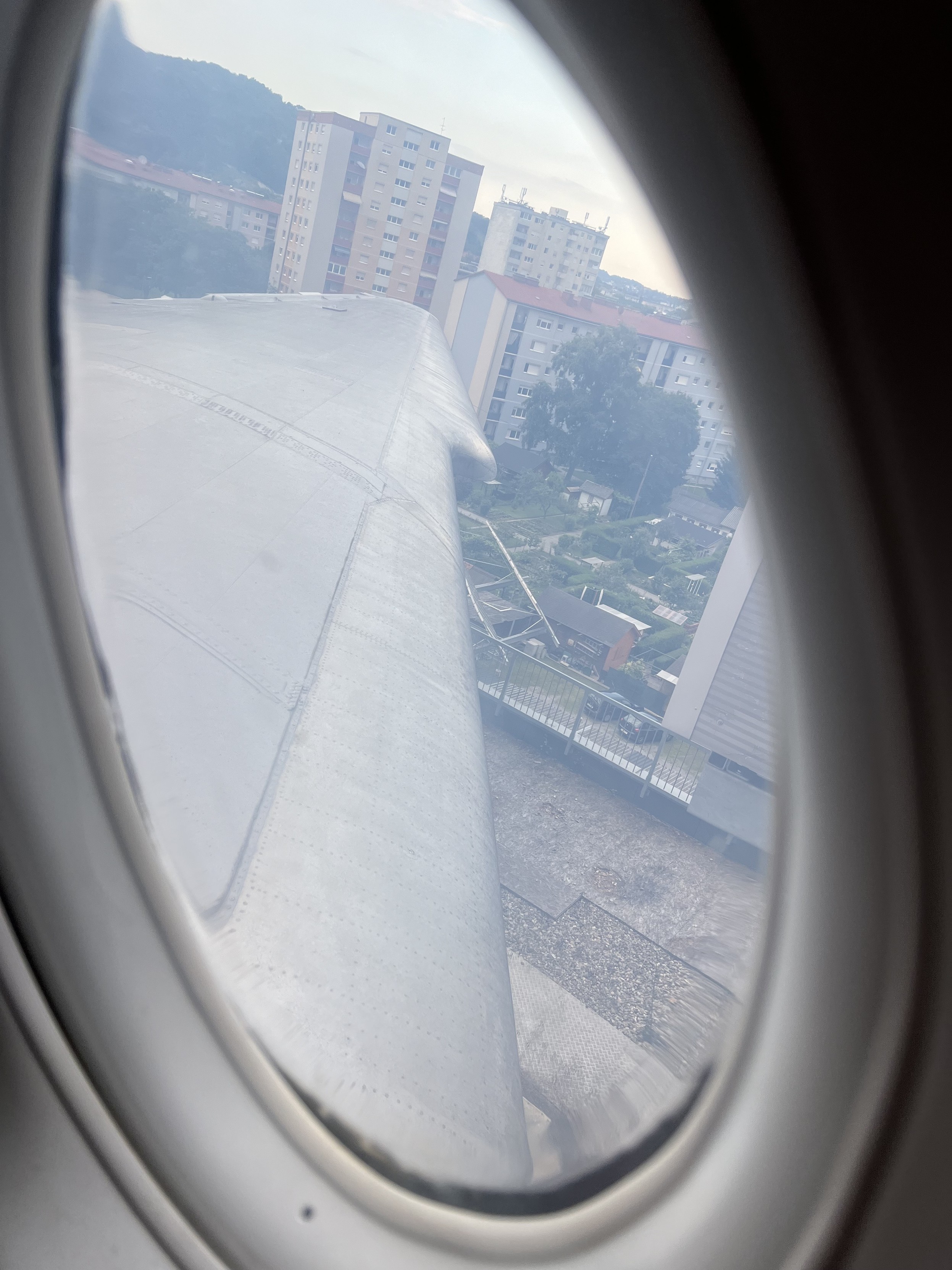 Blick aus einem Flugzeugfenster auf die Tragfläche des Flugzeugs und mehrere Wohngebäude in einer Stadt.