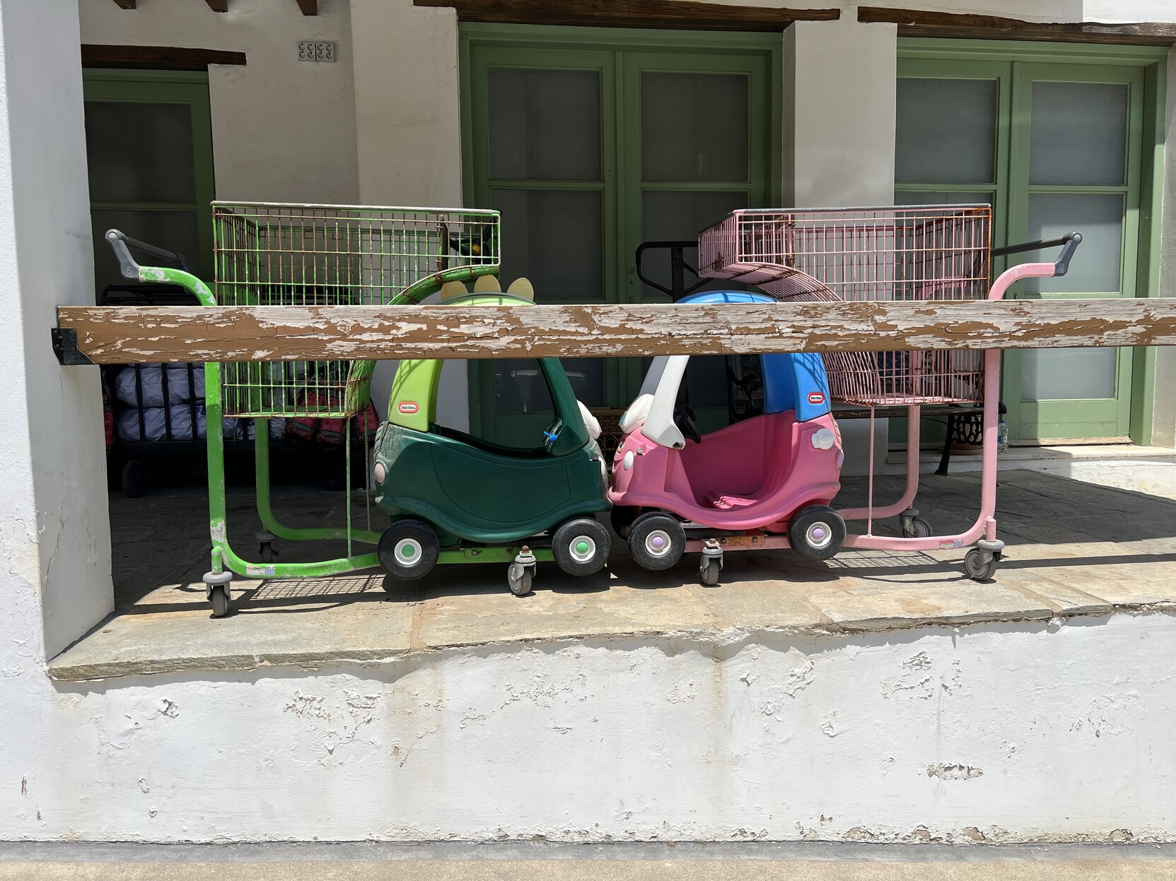 Zwei Einkaufswagen in denen kleine Plastikautos für Kinder vorne integriert sind. Die beiden Wägen stehe so zueinander, sodass es wirkt als wären die Autos zusammengestoßen. 