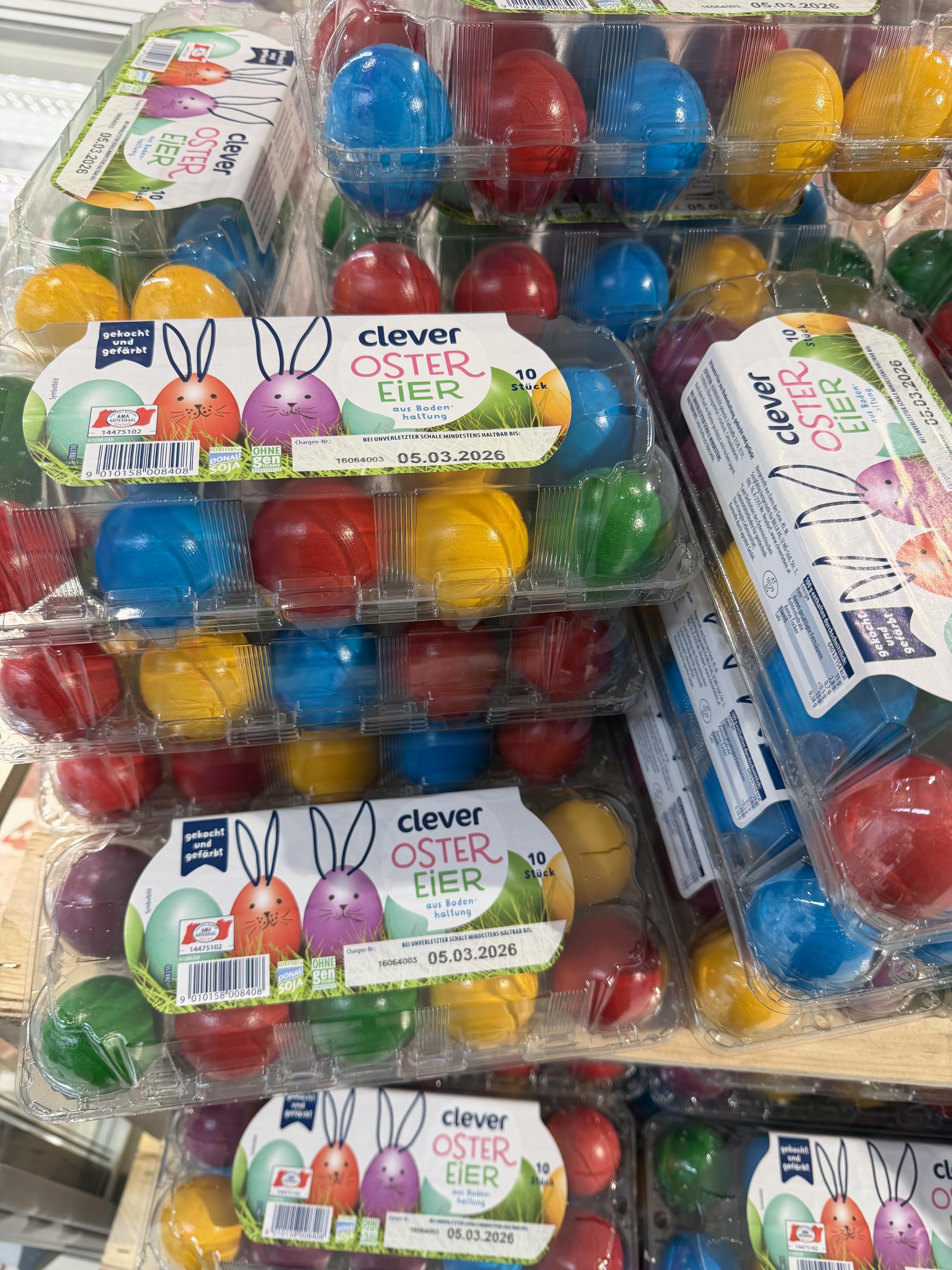 Stapel von durchsichtigen Eierschachteln mit bunten Eiern. Auf den Schachteln steht „Ostereier“ und ein Ablaufdatum „05.03.2026“