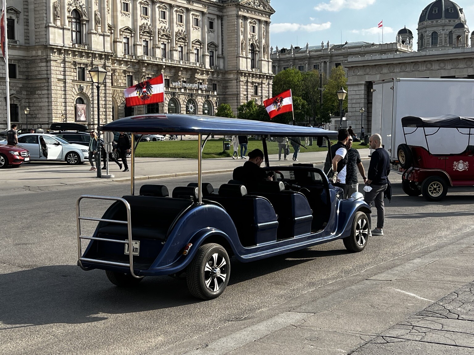 Offener Wagen mit mehreren Sitzreihen. Am Dach zwei Österreich-Flaggen mit Bundesadler