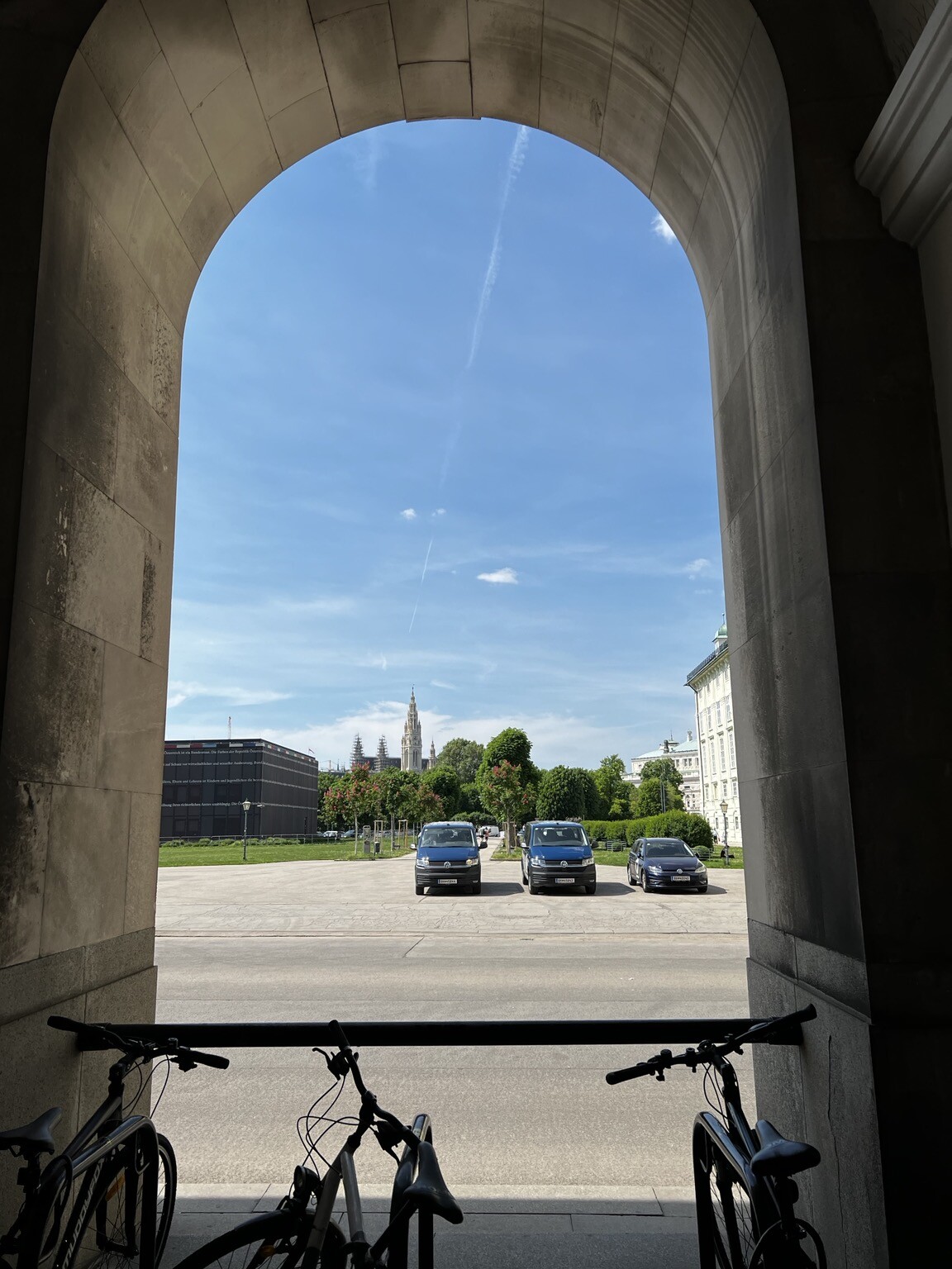 Blick durch Torbogen auf Heldenplatz, Bäume und dahinter das Wiener Rathaus