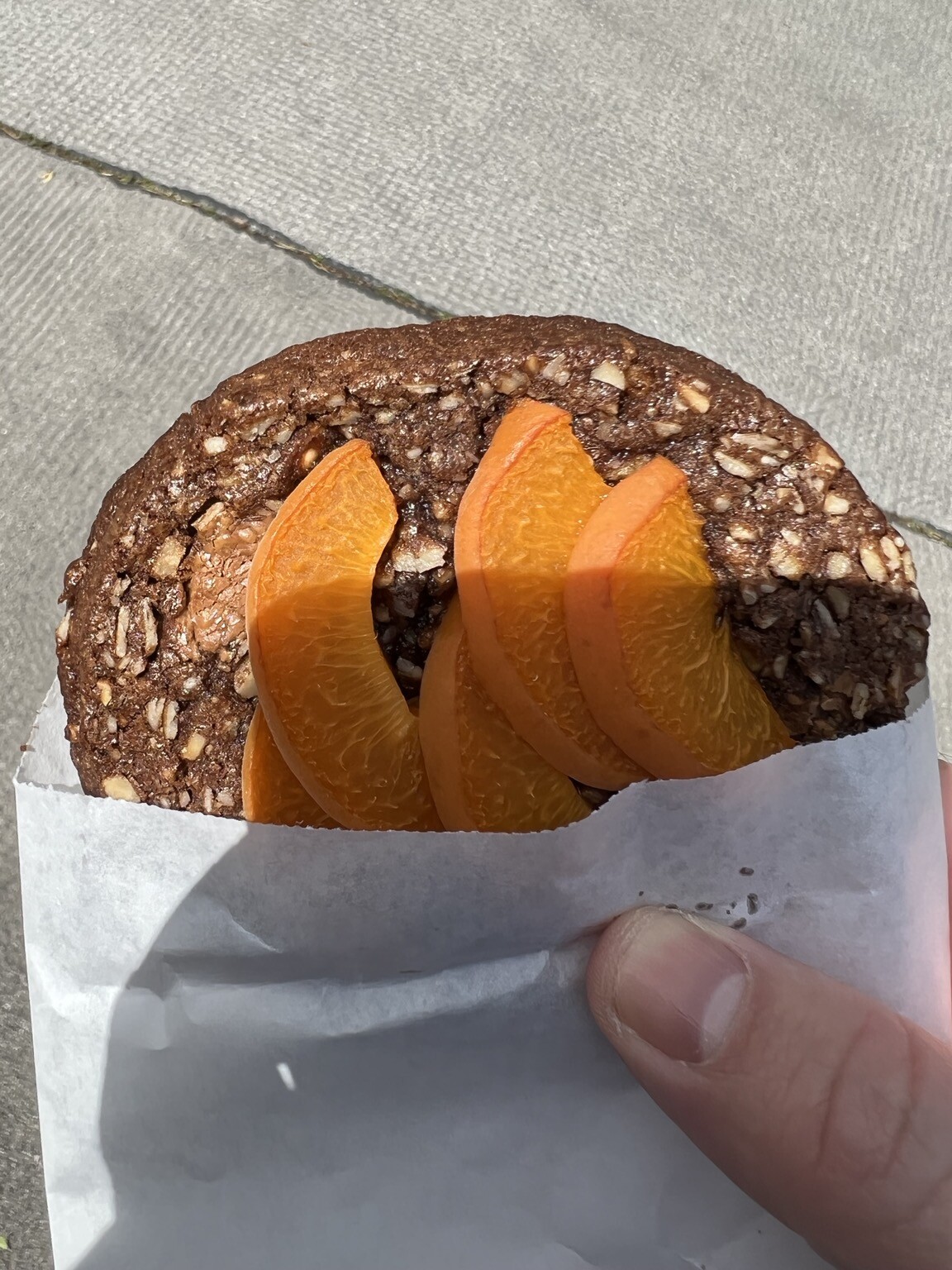 Großes Cookie mit Früchten belegt. Halb in Papierhülle steckend. Von Hand gehalten.