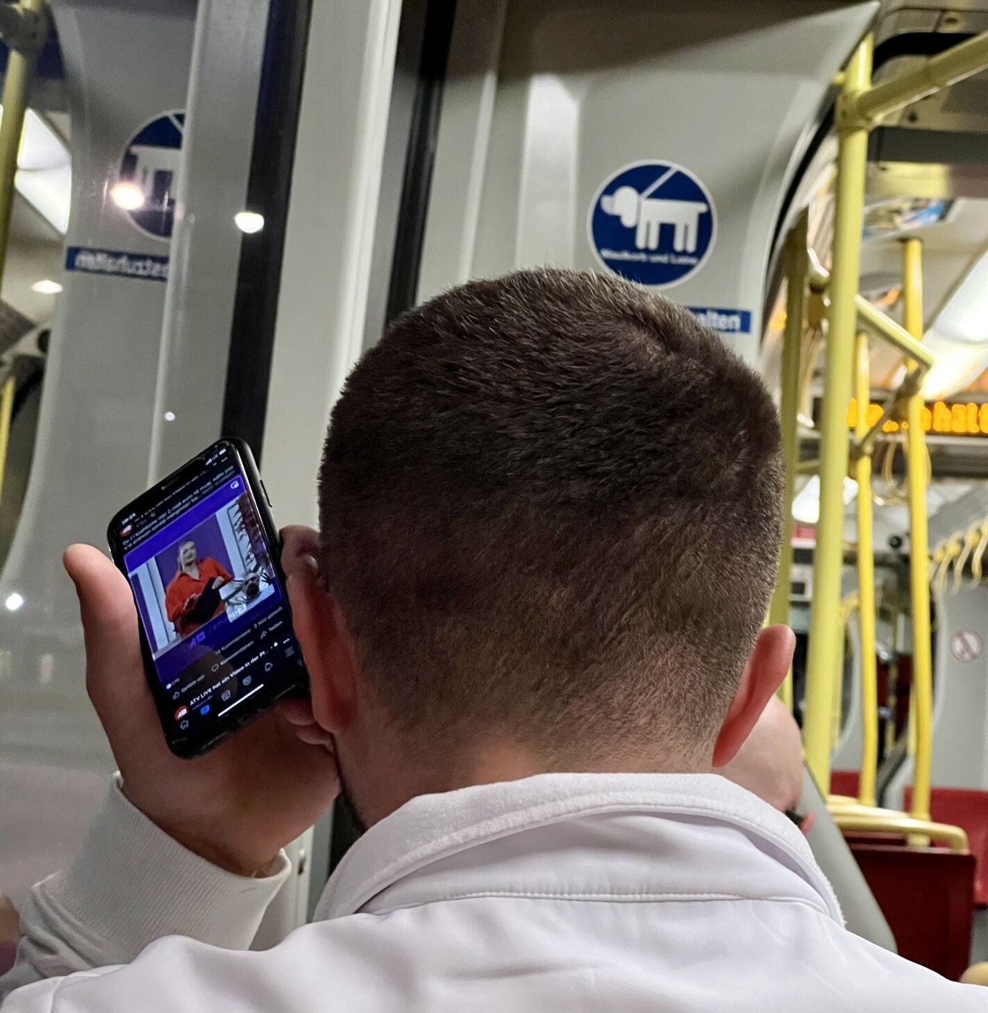 In der Straßenbahn. Mann von hinten. Hält Smartphone mit der Unterseite an sein Ohr.