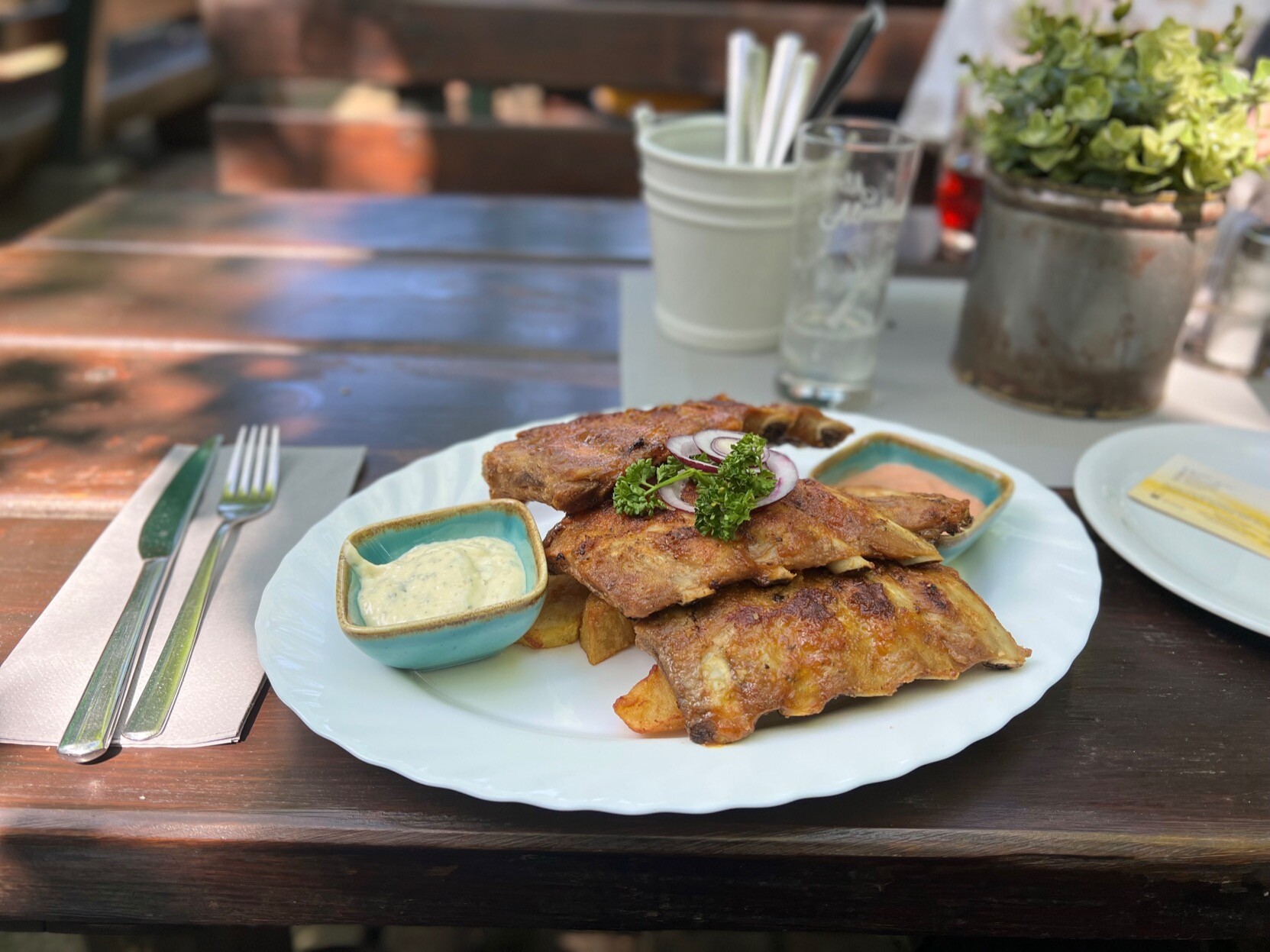 Spareribs mit Soßenschüsseln. Daneben ein Essbesteck auf Serviette.