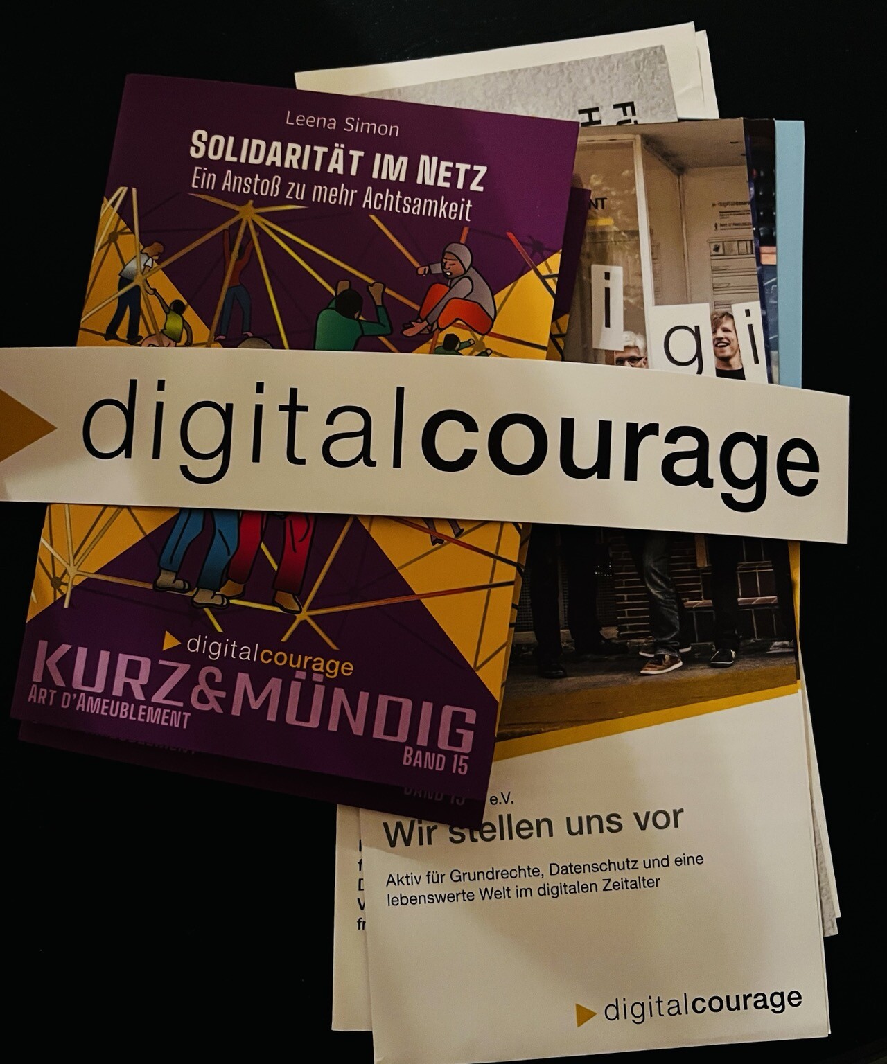 Broschüren übereinanderliegend. Darüber großer Kleber „digitalcourage“