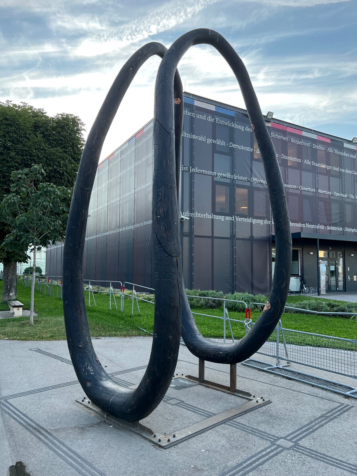 Holzskulptur eines großen in der Hälfte zum Boden gekrümmten Ringes.