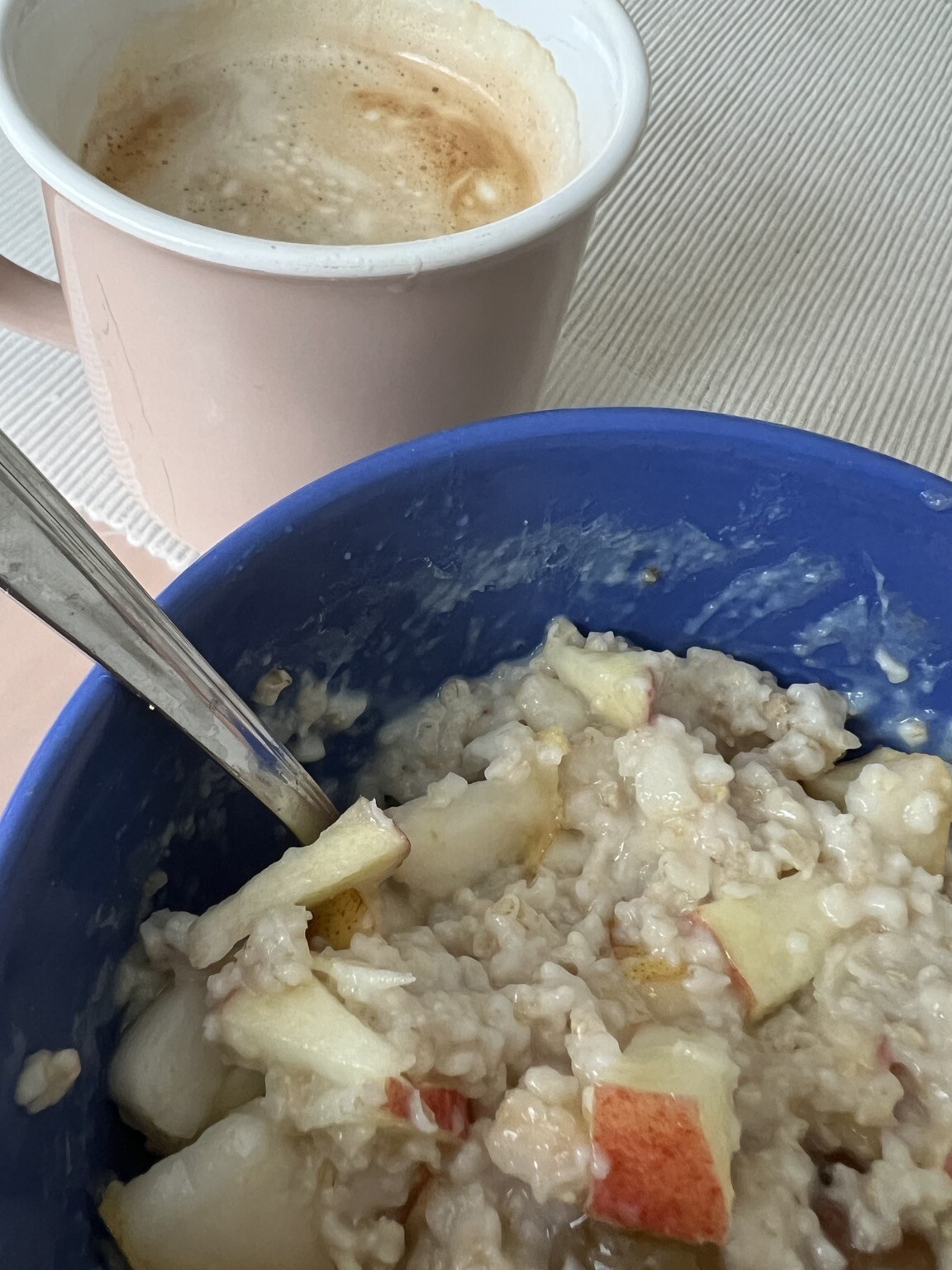 Schale mit Porridge und Fruchtstücken. Löffel steckt. Dahinter Kaffeehäferl.