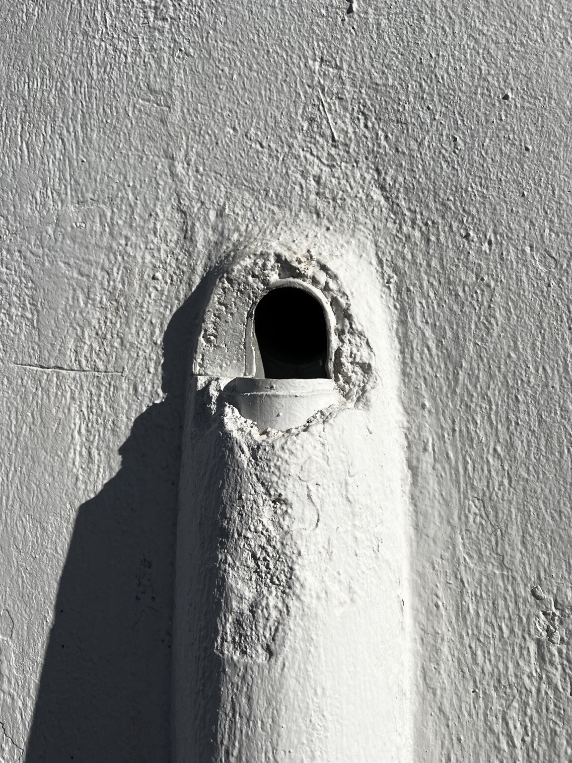 Rohr ein Stück aus der Mauer kommend. Darunter senkrecht verlaufendes Rohr, in Mauer verputzt.